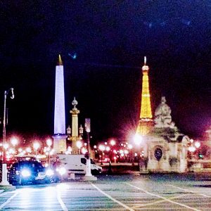 A night-time view of Place de la Concorde in Paris showing headlights of a car, the obelisk, the Eiffel Tower and the statue of Lille.