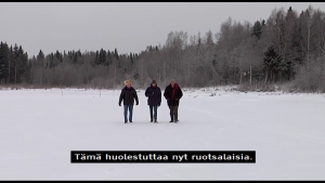 Screenshot from a television documentary of a wintry scene where three people walk towards the camera at a middle distance in a snow-covered open space with a forest in the background. There is a machine-translated subtitle in Finnish at the bottom of the screen that says: “Tämä huolestuttaa nyt ruotsalaisia.” The English translation of the subtitle is “This is now causing concern to Swedes.”