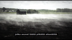 Screenshot from a television documentary of a misty field with a small wooden building in the middle and trees in the background. There is a machine-translated subtitle at the bottom of the screen in Finnish that says: “jotka asuvat täällä pitkällä aikavälillä.” The English translation of the subtitle is “who live here in the long term.”